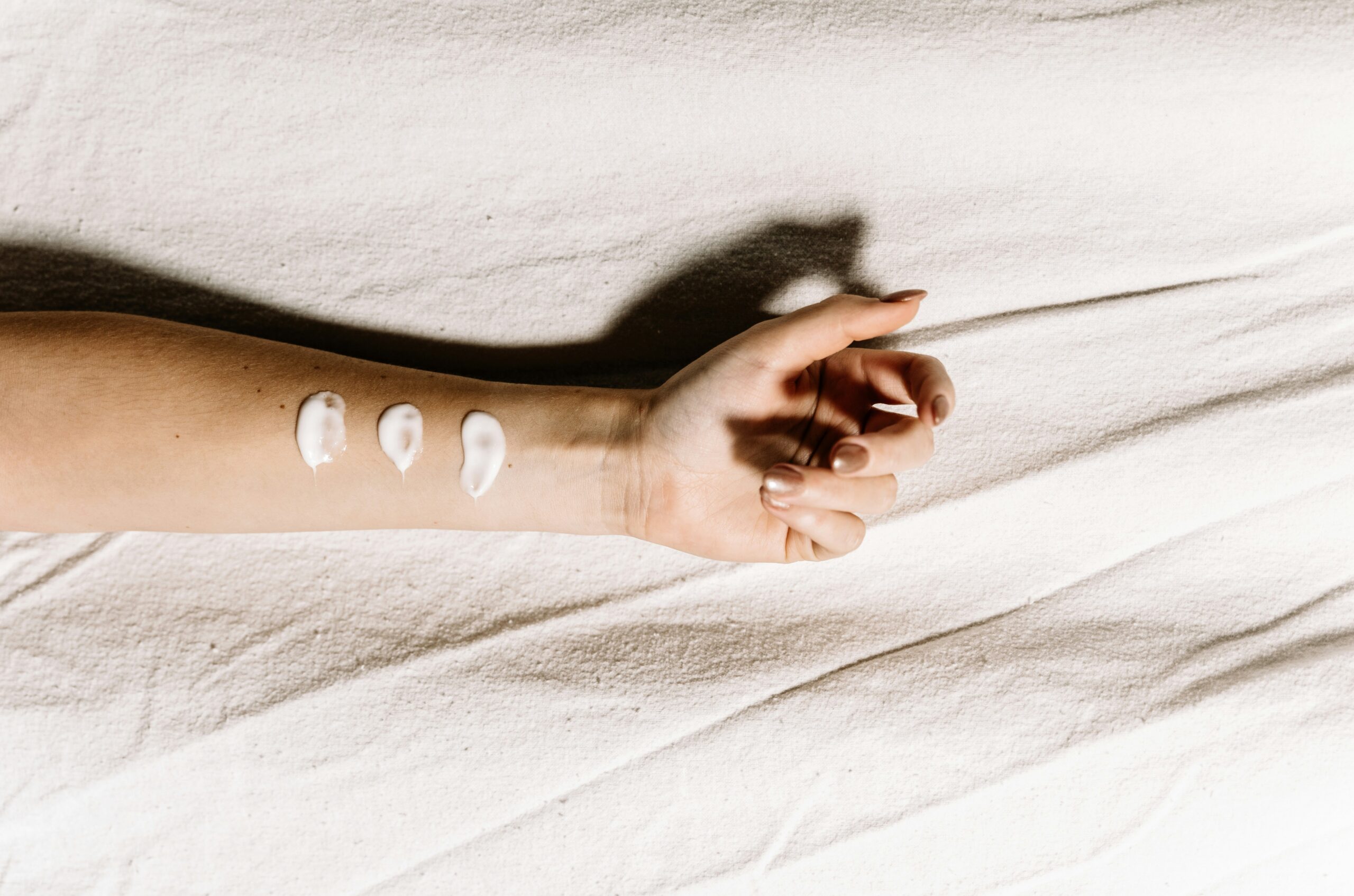 Female forearm resting on a light fabric with three swatches of white cream on the skin, showing retinol vs retinal textures.