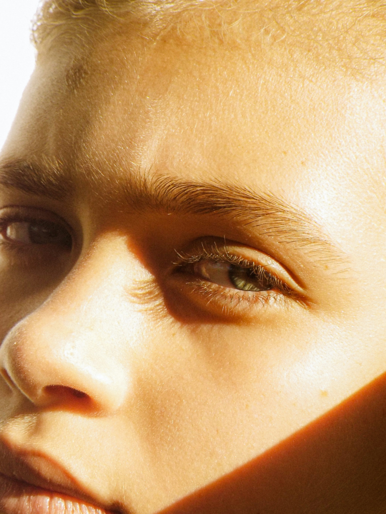 Close-up of a young woman’s face in warm sunlight, showing natural skin texture and glow, used to illustrate how hormones influence the skin.