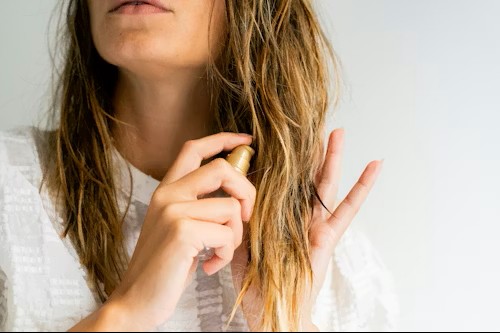 Woman applying a leave-in hair treatment to dry lengths as part of a gentle haircare routine