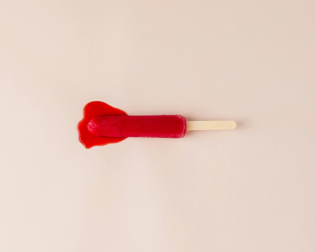 Red ice lolly melting on a beige background, symbolising the menstrual cycle and hormonal changes that affect the skin