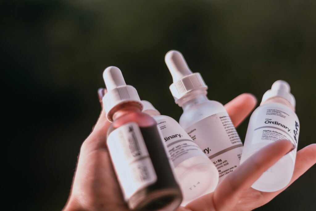 A hand holding four The Ordinary serum bottles with visible ingredient labels — illustrating how to read cosmetic ingredient list